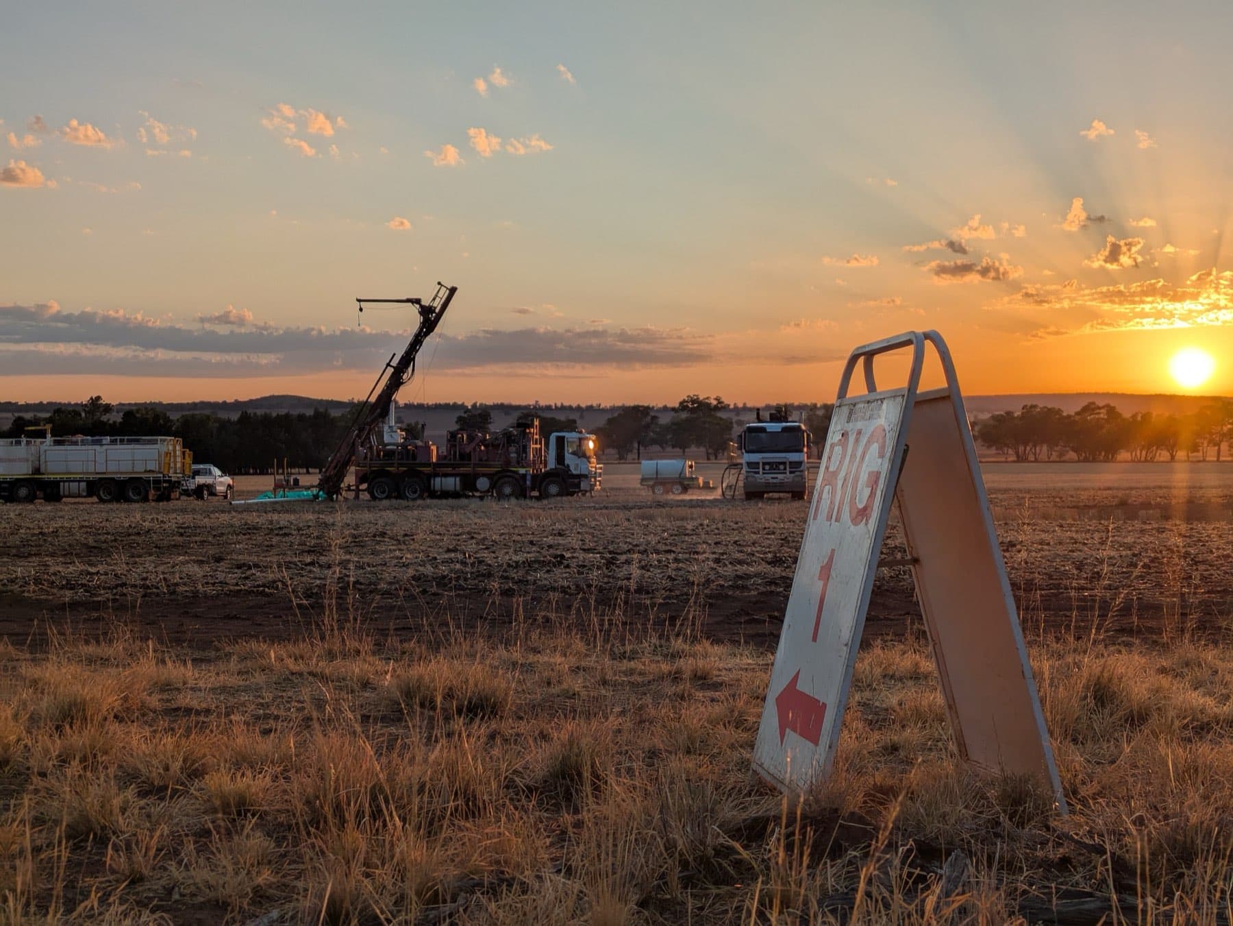 An exploration drill rig working at sunset behind a rig access sign.