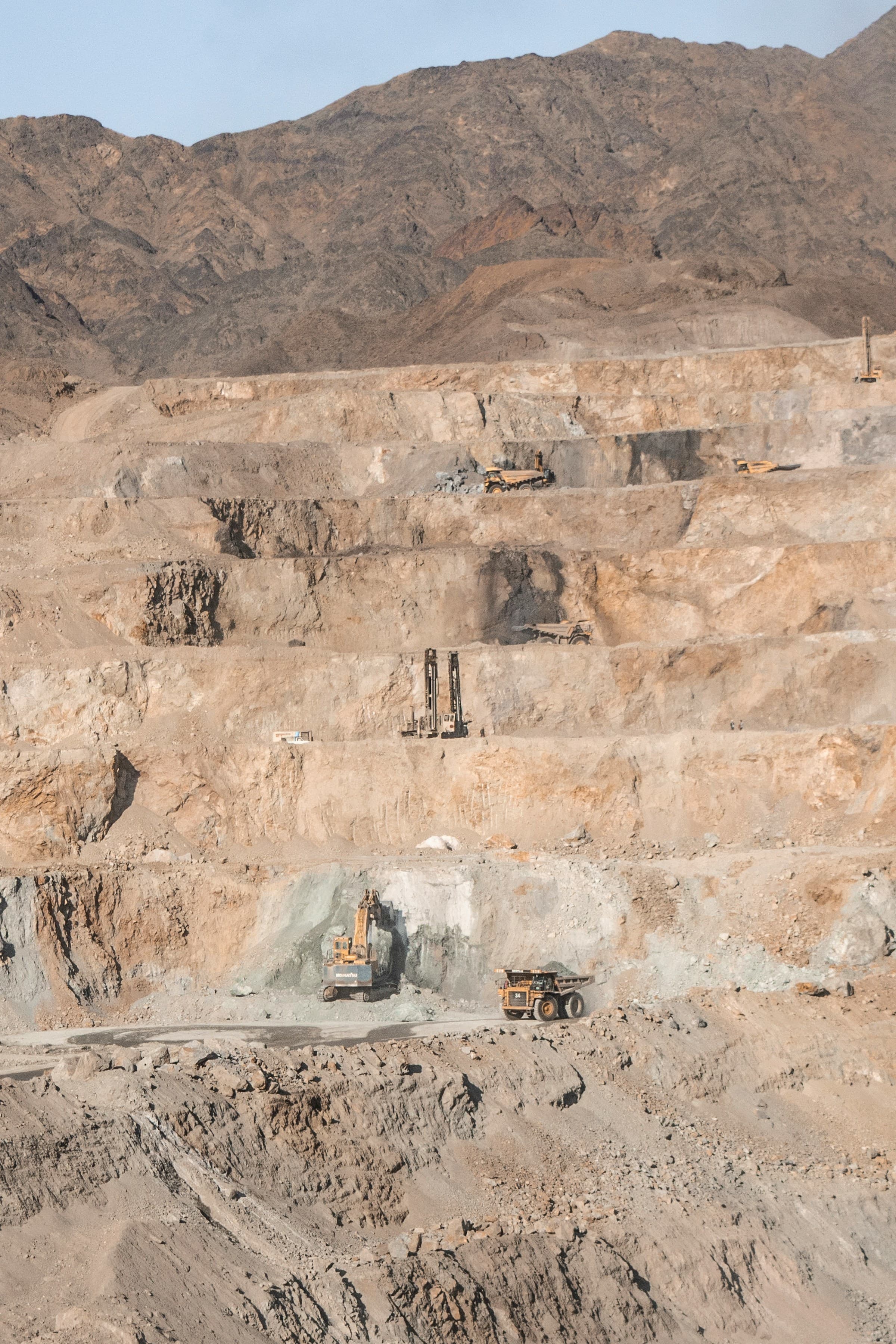 Wide view of a working quarry face with cut benches and haul roads