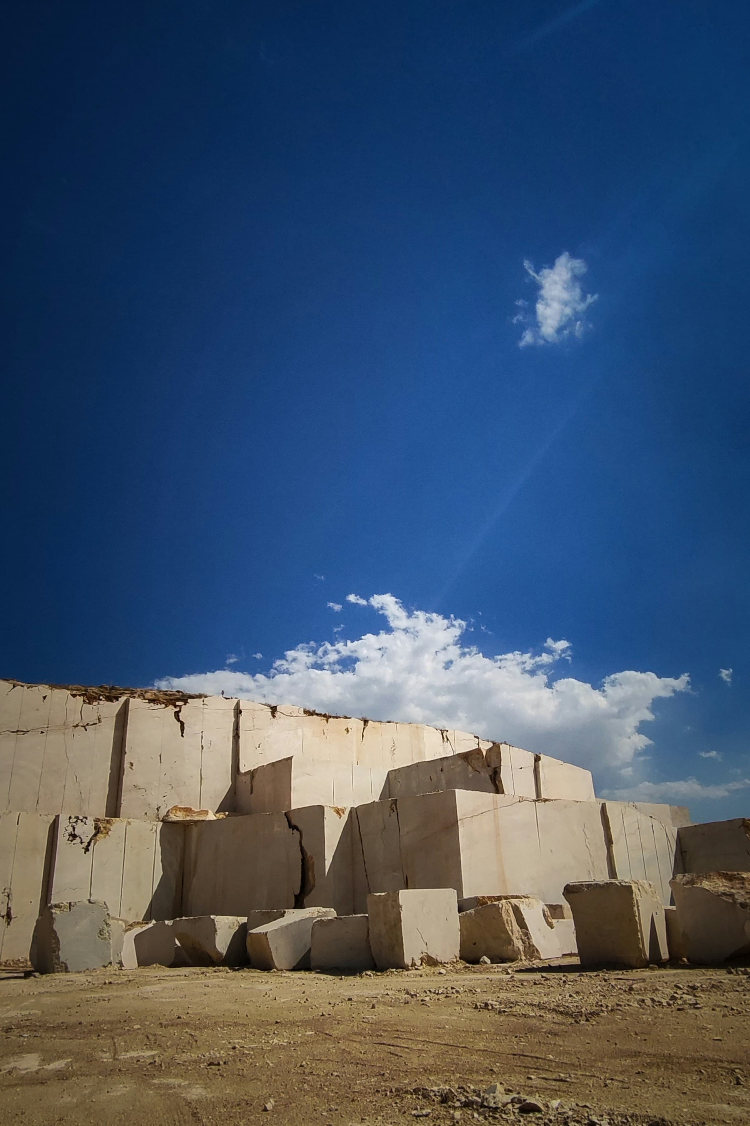 Cut stone blocks stacked at the foot of a quarry face under a clear sky